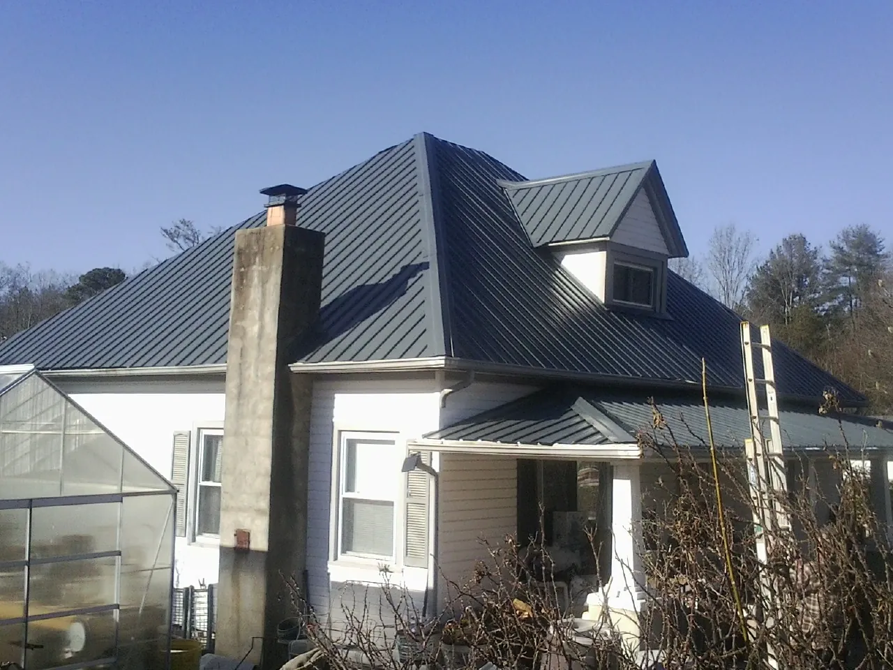 Dark blue standing seam metal roof on a white farmhouse with dormer — Slate & Tile Roof Repair by Roofing Brothers in Dolomite
