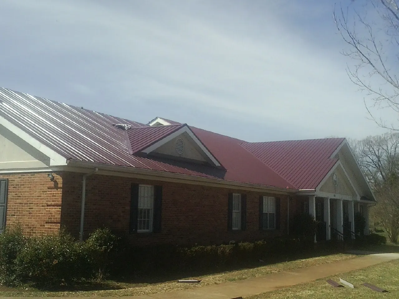 Red metal roof with gabled entries on a long brick building, from a Hail Damage Roof Repair job in Dolomite