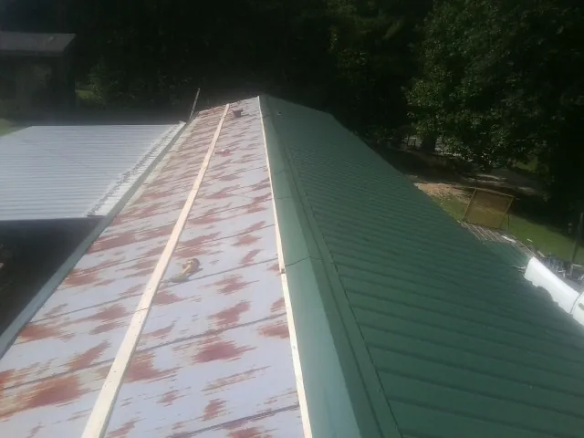 Old rusted panels beside newly installed green metal roofing — Wind Damage Roof Repair by Roofing Brothers in Dolomite