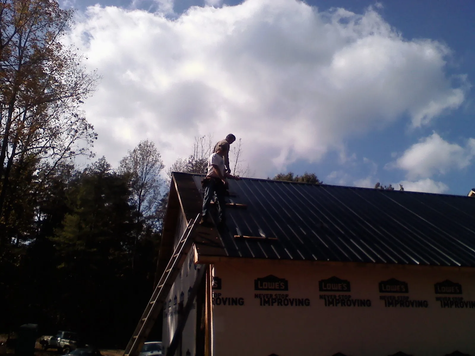 Roofer fastening dark metal panels high against a cloudy sky, from a Roof Inspection job in Dolomite