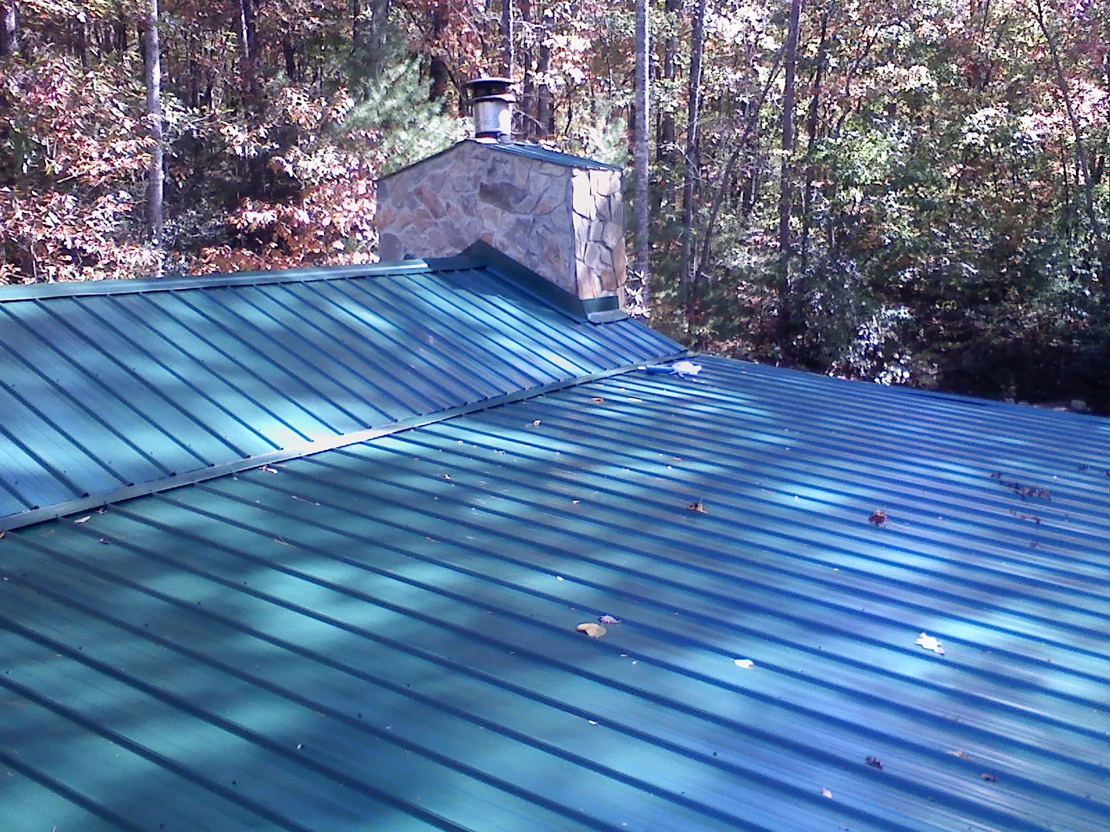New green metal roof and stone chimney surrounded by autumn woods in Dolomite
