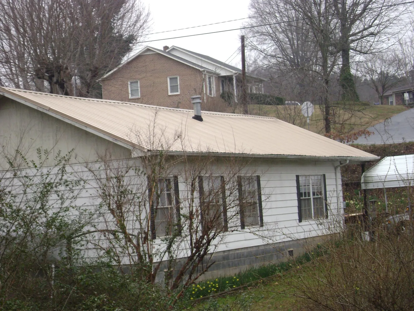 Tan metal roof on a white sided house set into a hillside — Commercial Roofing by Roofing Brothers in Dolomite